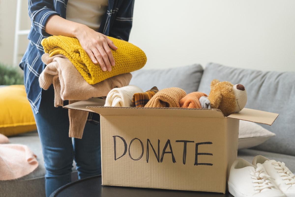 woman putting clothes and blankets into a cardboard box labeled "donate"