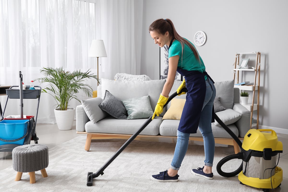 professional house cleaner vacuuming a rug in a living room