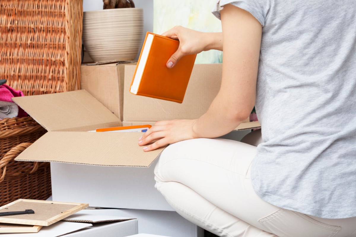 person kneeling down and packing books into a box