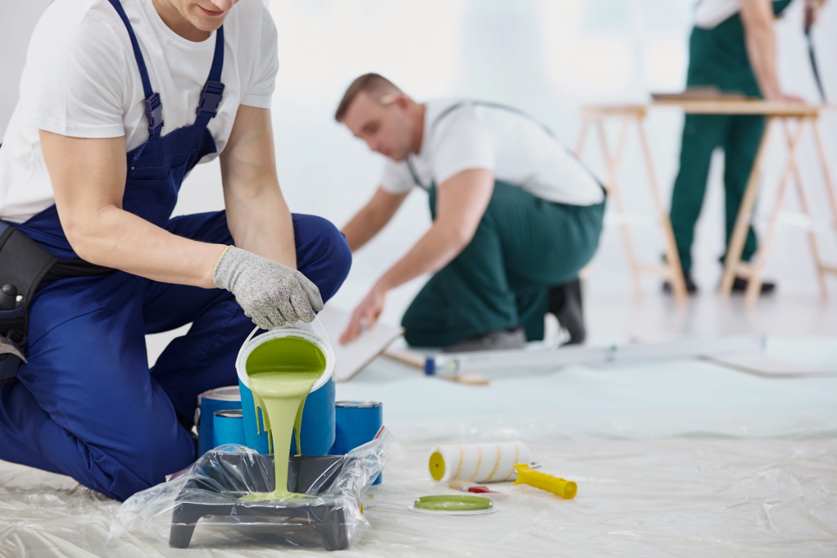 crew of three men prepping and painting a room; one pouring green paint into tray
