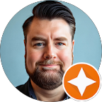 A professional portrait of Christopher Gravelyn, a man with dark hair and a beard, smiling slightly. An orange review icon is visible in the corner.